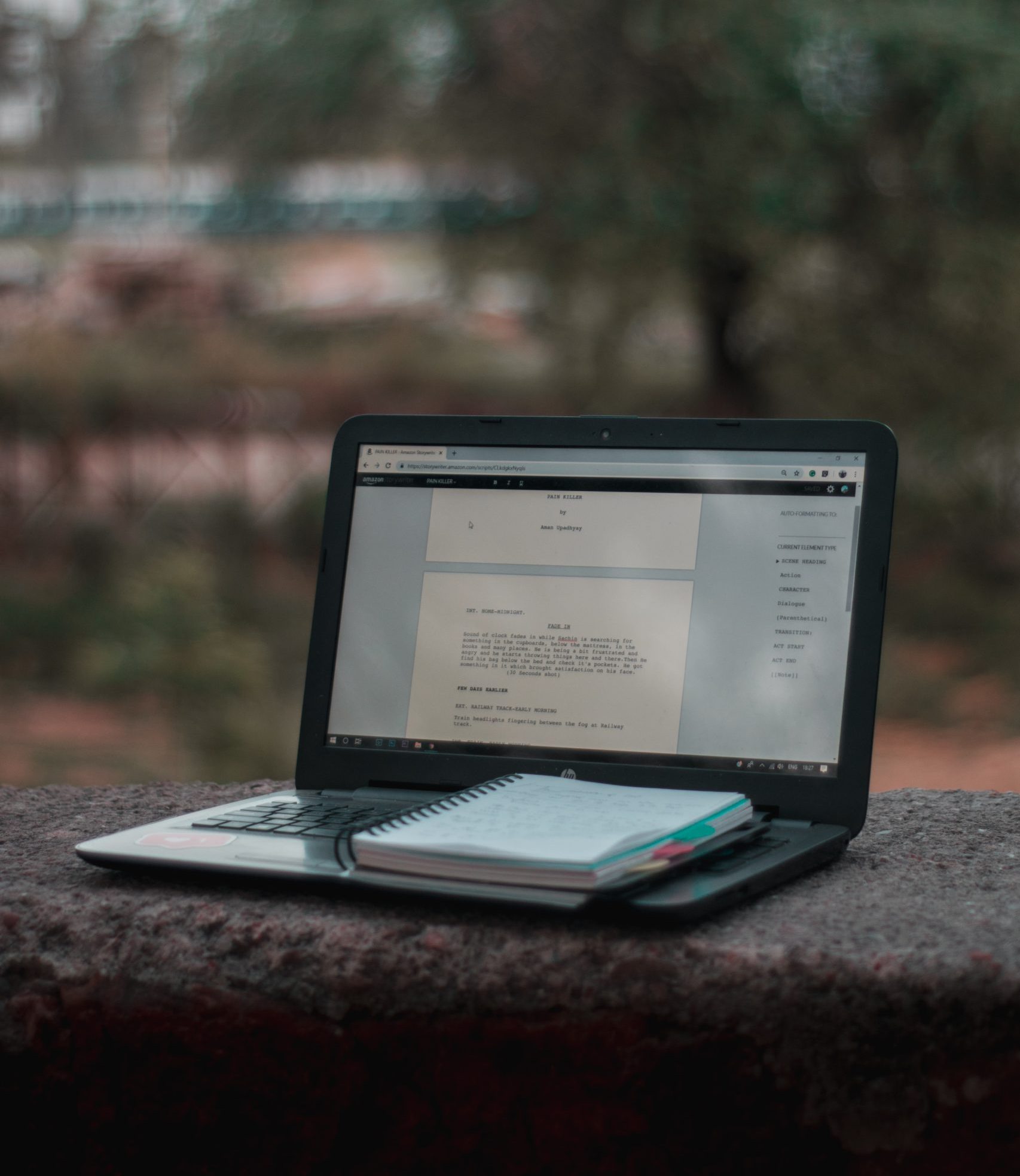 Laptop and notebook on stone wall outdoors.