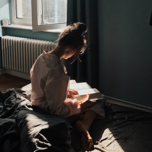 Woman reads a book on a bed bathed in sunlight. Here’s why book banning is bad by Publish Your Purpose.