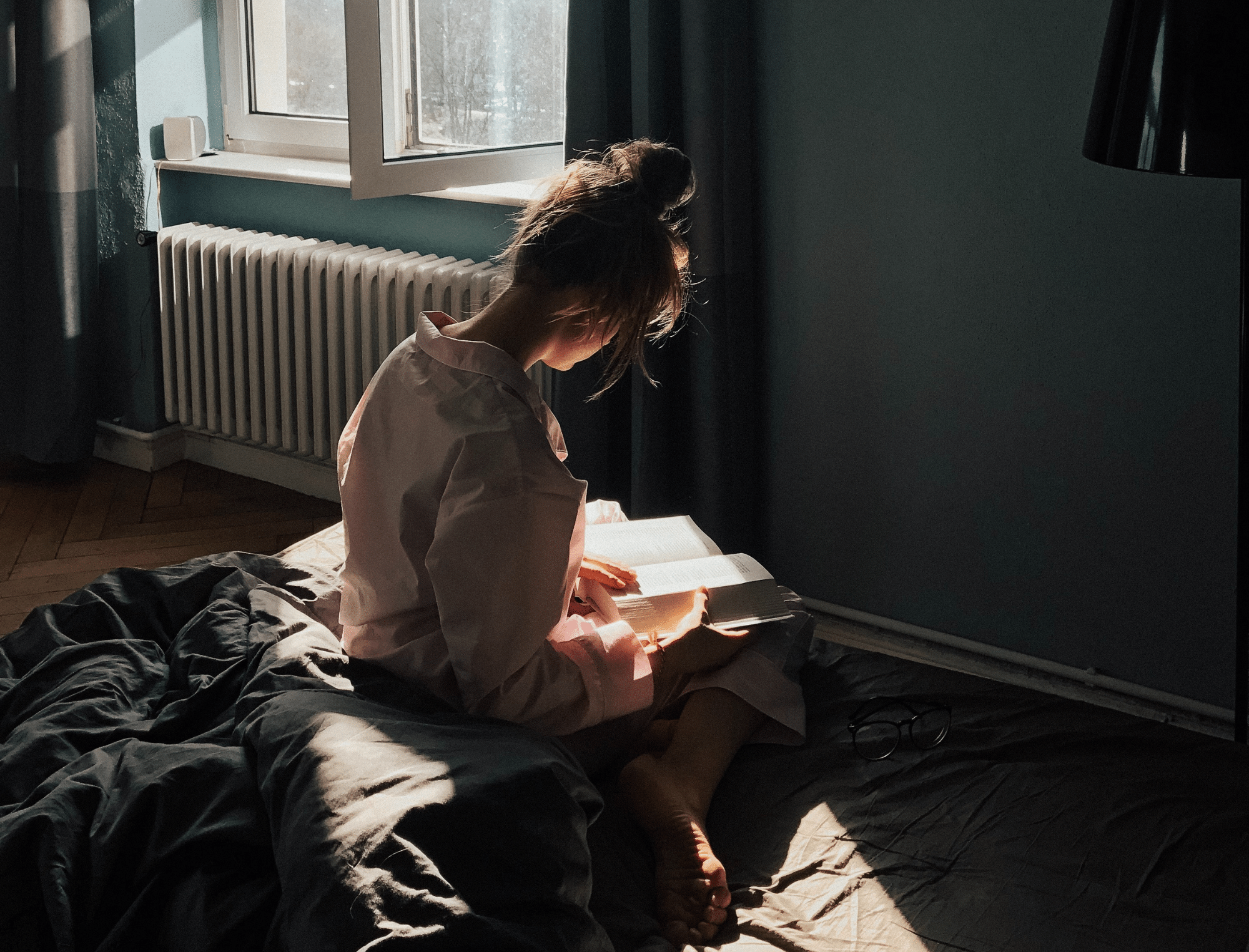 Woman reads a book on a bed bathed in sunlight. Here’s why book banning is bad by Publish Your Purpose.